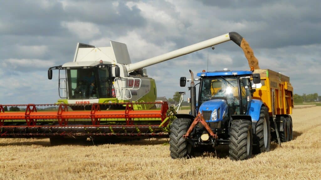 En skurtresker og traktor som høster korn. Traktor kjørende på landbruksdekk.